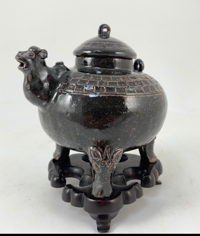 An unusual Chinese black ware tenmoku glazed tripod wine pot, 19th/20th century, with camel head spout, zoomorphic feet, 14cm high, hongmu stand